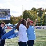 Coach Brandon Hull in white jersey gets help signaling the defensive secondary positioning for the next play.